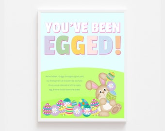 Peut inclure: Une affiche imprimable avec le texte "You've Been Egged!" en lettres colorées. L'affiche représente un lapin de dessin animé tenant des œufs de Pâques colorés et le texte "We've hidden 12 eggs throughout your yard, but finding them all shouldn't be too hard. Once you've collected all of the treats, egg another house down the street!"