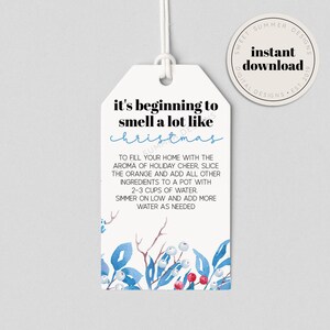 Könnte beinhalten: Weißer Geschenkanhänger mit blauem und rotem Blumendesign. Der Text lautet "it's beginning to smell a lot like christmas" und enthält Anweisungen für die Herstellung eines Potpourris mit Orangenscheiben und anderen Zutaten.