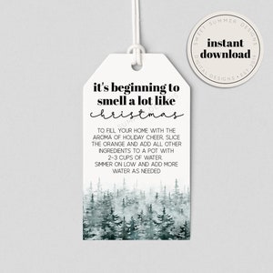 Könnte beinhalten: Ein weißer, druckbarer Geschenkanhänger mit einem Aquarell-Waldhintergrund. Der Text lautet "It's beginning to smell a lot like Christmas" und enthält Anweisungen für die Herstellung eines Schmortopfs, um Ihr Zuhause mit dem Aroma von festlicher Stimmung zu füllen.