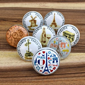 Peut inclure: Un ensemble de huit boutons de placard ronds en céramique avec divers motifs imprimés liés à Paris, en France. Les graphismes incluent la tour Eiffel, une bouteille de vin, un vélo, l'Arc de Triomphe et le texte Paris, France et Je t'aime.