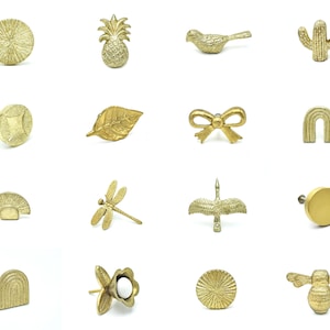 May include: Assortment of gold-toned metal drawer pulls in various shapes, including a pineapple, a bird, a cactus, a leaf, a bow, a rainbow arch, a dragonfly, a crane, a circle, a half-circle, a flower, a bee, and a sunburst.