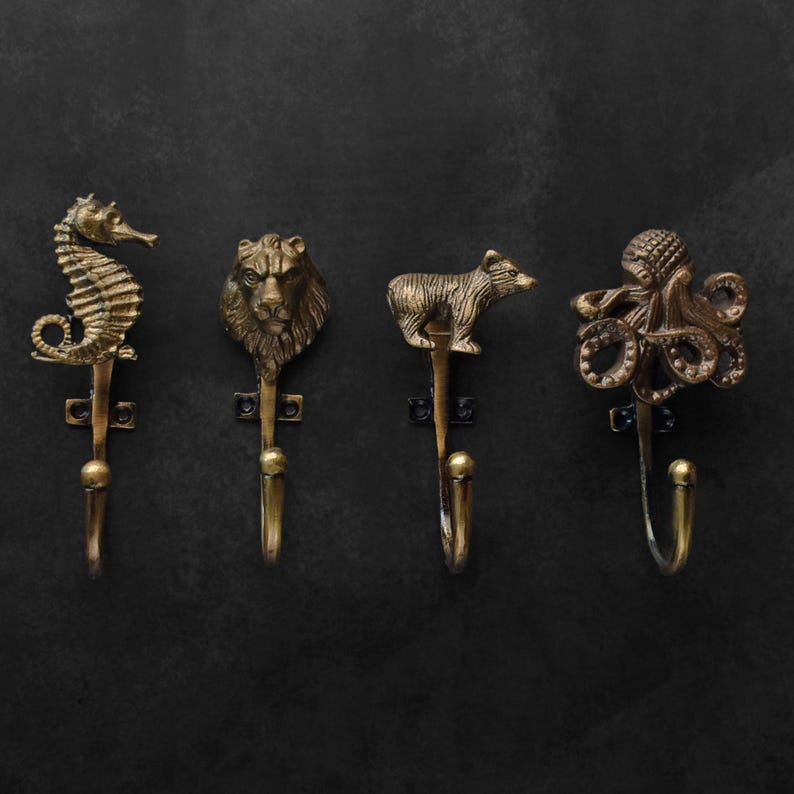 Peut inclure: Quatre crochets muraux en laiton antique avec des motifs d'animaux : un hippocampe, une t&ecirc;te de lion, un ours et une pieuvre. Chaque crochet a une figurine d'animal d&eacute;corative en haut et un crochet incurv&eacute; en dessous. Les crochets sont mont&eacute;s sur un fond sombre.