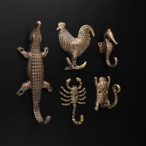 May include: Five bronze-colored animal-shaped hooks. The hooks include an alligator, rooster, seahorse, scorpion, and tiger. Each hook is detailed with textured surfaces and is mounted on a black background.