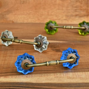 May include: Three decorative cabinet knobs with a starburst design. The knobs are made of glass and have a brass base. The knobs are in blue, green, and clear.