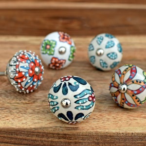 Puede incluir: Cinco pomos de cer&aacute;mica con coloridos patrones florales. Los pomos son blancos con varios colores, incluyendo rojo, naranja, azul, verde y amarillo. Cada pomo tiene un tornillo de metal plateado.
