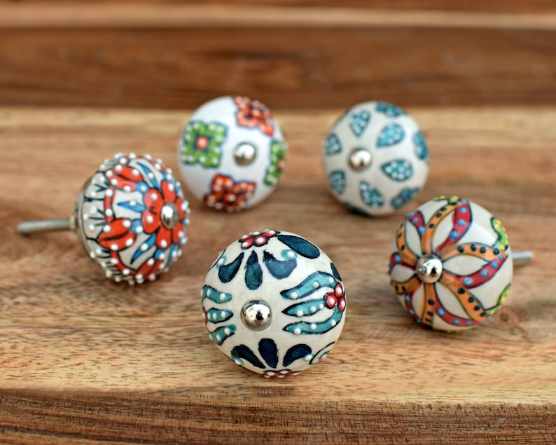 Puede incluir: Cinco pomos de cer&aacute;mica con coloridos patrones florales. Los pomos son blancos con varios colores, incluyendo rojo, naranja, azul, verde y amarillo. Cada pomo tiene un tornillo de metal plateado.