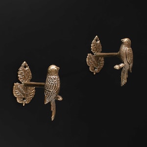 Peut inclure: Deux patères murales assorties en métal de couleur bronze. Chaque crochet présente une figurine d'oiseau détaillée perchée sur une branche s'étendant depuis une base en forme de groupe de trois feuilles texturées avec des trous de vis.
