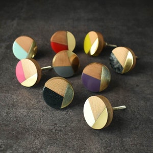 May include: Assortment of nine round wooden knobs with geometric patterns and gold accents. Each knob features a different colour combination, including teal, pink, red, grey, purple, black, and yellow.