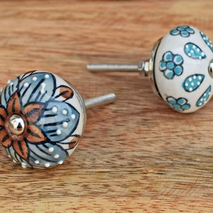 Puede incluir: Dos pomos de caj&oacute;n de cer&aacute;mica con dise&ntilde;os florales. Un pomo presenta un patr&oacute;n floral azul y marr&oacute;n, mientras que el otro tiene un fondo blanco con acentos florales azules y blancos.