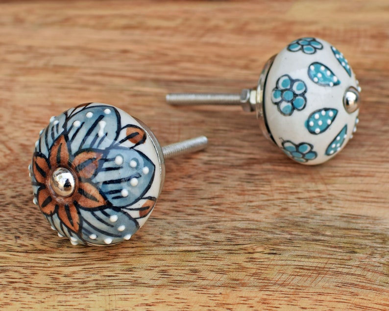 Puede incluir: Dos pomos de caj&oacute;n de cer&aacute;mica con dise&ntilde;os florales. Un pomo presenta un patr&oacute;n floral azul y marr&oacute;n, mientras que el otro tiene un fondo blanco con acentos florales azules y blancos.