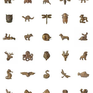 Peut inclure: Une collection de petites figurines d'animaux de couleur bronze, comprenant un &eacute;l&eacute;phant, un hibou, un cerf, une libellule et un hippocampe. Les miniatures d&eacute;taill&eacute;es sont dispos&eacute;es sur fond blanc, pr&eacute;sentant diverses formes de la faune.