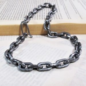 Pu&ograve; includere: Una collana a catena argentata realizzata in metallo spesso e collegato. La catena &egrave; composta da maglie ovali.