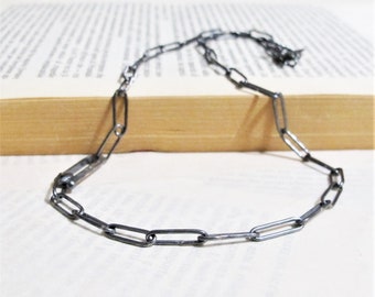 Può includere: Una collana a catena d'argento con un designo semplice e collegato. La catena è composta da piccoli anelli rettangolari.