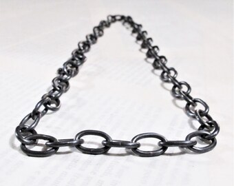 Può includere: Una collana a catena d'argento con maglie ovali. La catena è appoggiata su una superficie bianca.