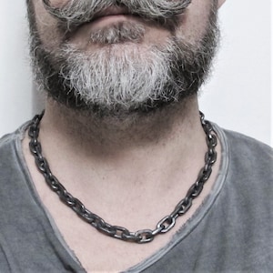 Pu&ograve; includere: Una collana a catena argentata realizzata in metallo spesso e collegato. La catena &egrave; indossata da una persona con barba e baffi grigi.