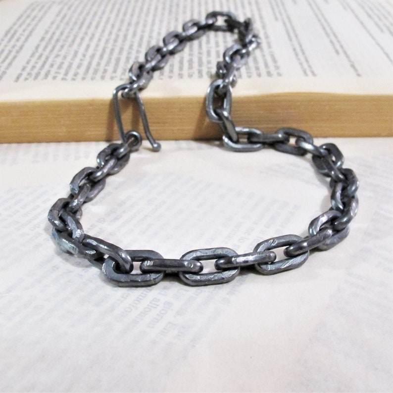 Pu&ograve; includere: Una collana a catena argentata realizzata in metallo spesso e collegato. La catena &egrave; composta da maglie ovali.