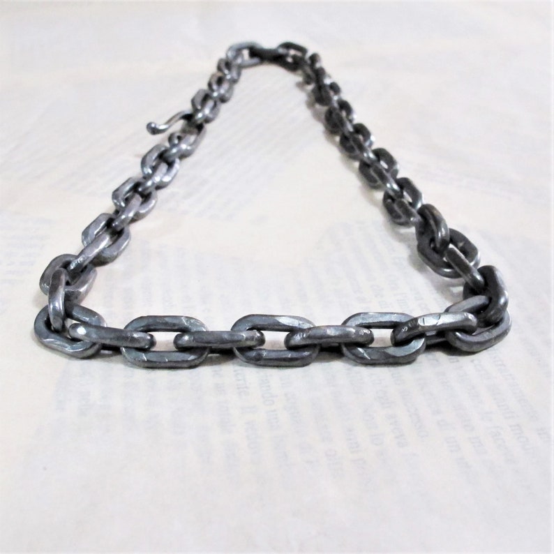 Pu&ograve; includere: Una collana a catena argentata realizzata in metallo spesso e collegato. La catena &egrave; composta da maglie ovali.
