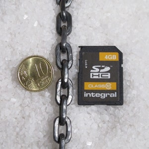Pu&ograve; includere: Primo piano di una catena argentata e una scheda di memoria SDHC da 4 GB di classe 10 del marchio Integral. La scheda di memoria &egrave; nera con testo bianco e un logo giallo.