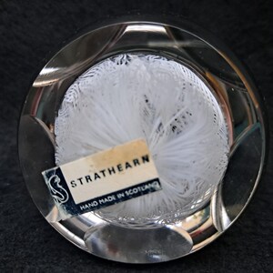 May include: A clear glass paperweight with a white, feathery design inside. The paperweight has a label that reads "Strathearn Hand Made in Scotland."
