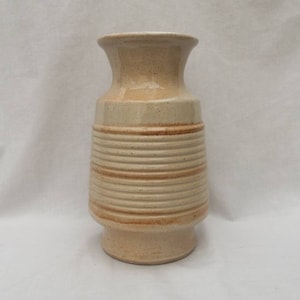 May include: A beige ceramic vase with brown stripes. The vase has a wide base and a narrow neck.