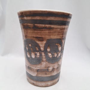 May include: A brown ceramic vase with a white glaze and a geometric pattern. The vase has a wide mouth and a narrow base.