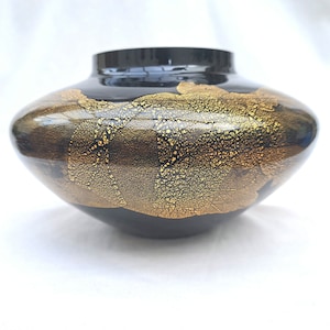 May include: A black ceramic vase with a wide, rounded base and a narrow opening. The vase is decorated with gold leaf accents in a swirling pattern.