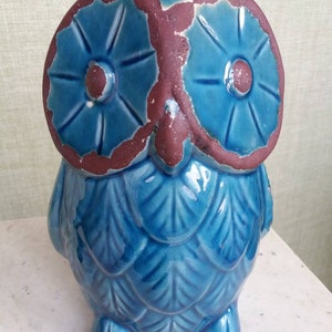Puede incluir: Una figurita de búho de cerámica azul con detalles marrones alrededor de los ojos. El búho tiene un patrón de plumas detallado en su cuerpo.