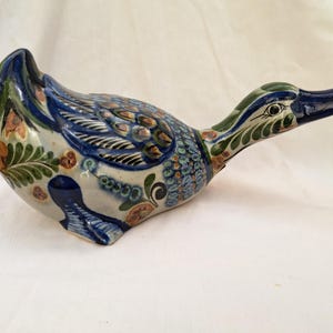 Op de afbeelding: Handbeschilderd keramiek eendenbeeldje met blauwe, groene en bruine bloemmotieven. De eend heeft een lange nek en een wit lichaam.