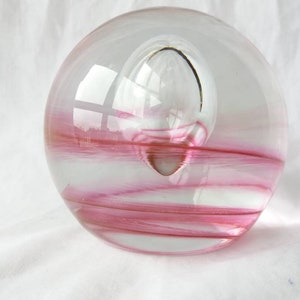 May include: A clear glass paperweight with pink swirls and a small bubble inside.