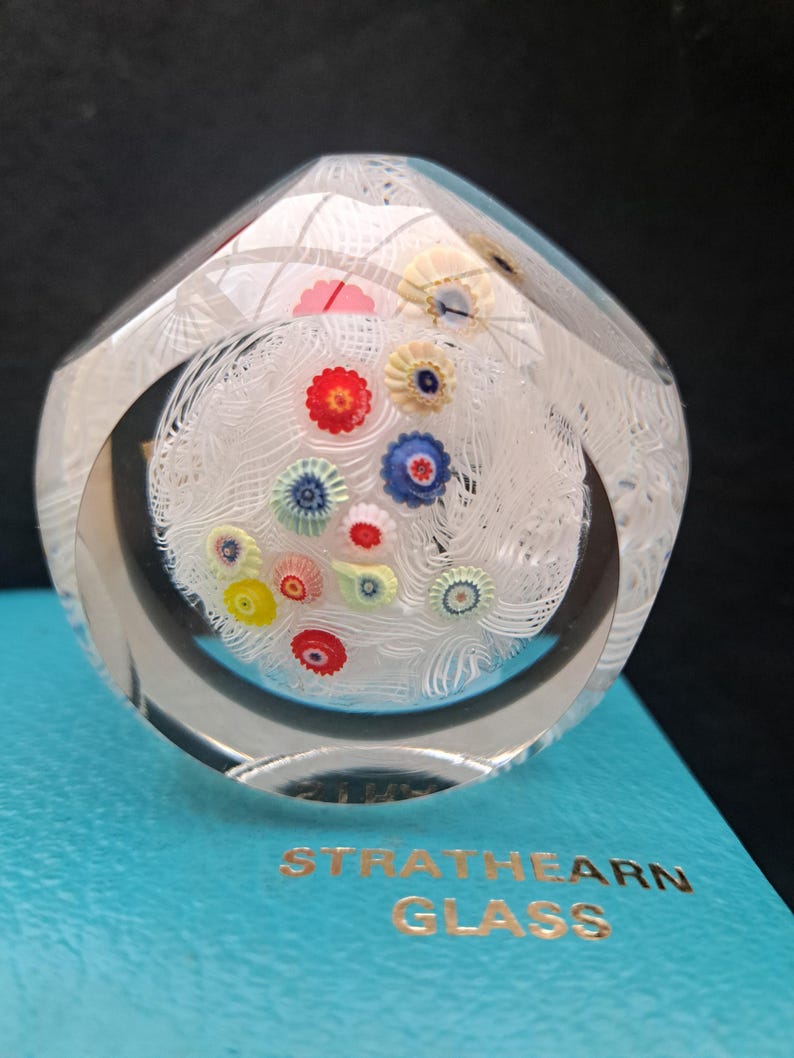 May include: A clear glass paperweight with a white swirl design and colorful flowers inside. The paperweight is on a blue box with the text "Strathearn Glass".