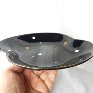May include: A black ceramic serving dish with a gold rim and a polka dot pattern in white, orange, and blue.