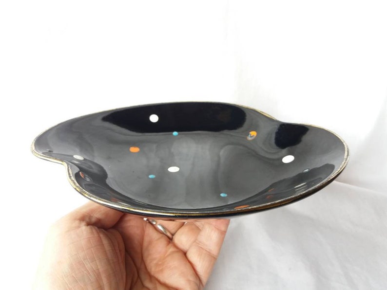 May include: A black ceramic serving dish with a gold rim and a polka dot pattern in white, orange, and blue.