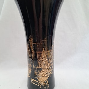 May include: A black glass vase with a flared top and a gold textured design. The vase has a glossy finish and a simple, elegant shape. The gold design appears to be applied in a textured, abstract pattern.