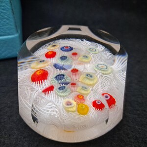 May include: A clear glass paperweight with white swirls and colorful flowers inside. The flowers are red, yellow, blue, and green.