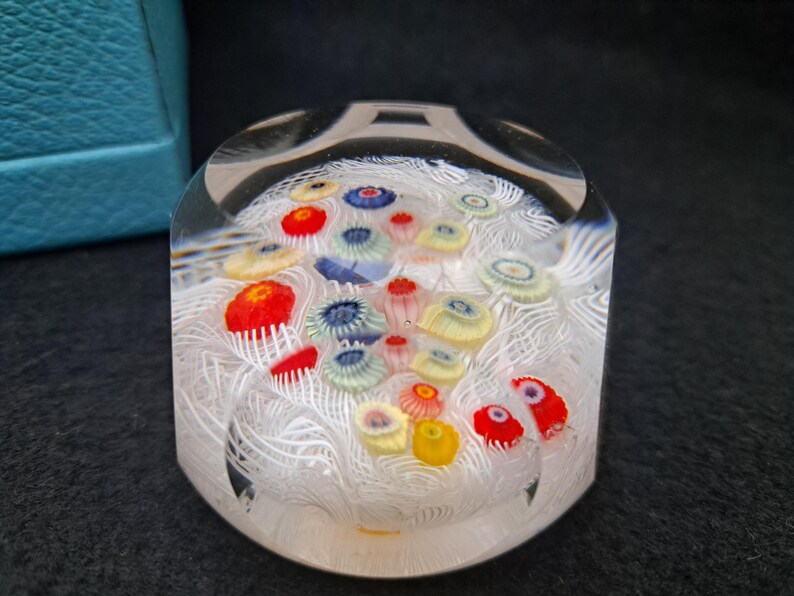May include: A clear glass paperweight with white swirls and colorful flowers inside. The flowers are red, yellow, blue, and green.