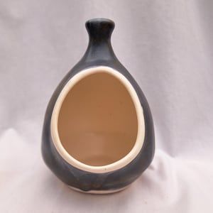Może przedstawiać: Ciemnoniebieska ceramiczna doniczka wisząca o zaokrąglonym korpusie i okrągłym otworze. Wnętrze jest beżowe, a obręcz obrysowana na biało. Doniczka ma wąską szyjkę i jest przeznaczona do eksponowania małych roślin lub kwiatów.