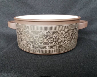 May include: A brown ceramic casserole dish with a white interior and a geometric pattern in gold. The pattern features circles with spokes and triangles.