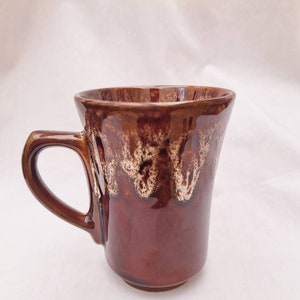 May include: A brown ceramic mug with a white glaze design. The mug has a rounded shape and a handle.