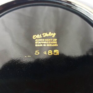 May include: Close-up of the bottom of a black ceramic plate with gold lettering. The text reads "Old Foley, James Kent Ltd, Staffordshire, Made in England, 5 4851".