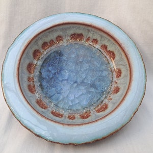 Puede incluir: Un cuenco de cerámica azul claro con un esmalte texturizado y craquelado. El cuenco tiene un borde marrón con un patrón decorativo.