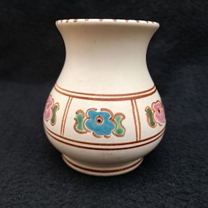 Może przedstawiać: Mały, biały ceramiczny wazon z brązową krawędzią i kwiatowym wzorem. Wazon ma zaokrąglone ciało i wąską szyjkę. Kwiaty są pomalowane w odcieniach różowego, niebieskiego i zielonego.