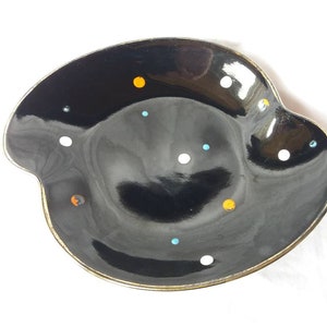 May include: A black ceramic dish with a gold rim and a speckled pattern of white, orange, and blue dots.