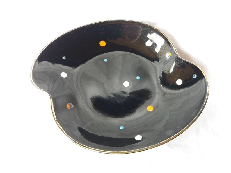 May include: A black ceramic dish with a gold rim and a speckled pattern of white, orange, and blue dots.
