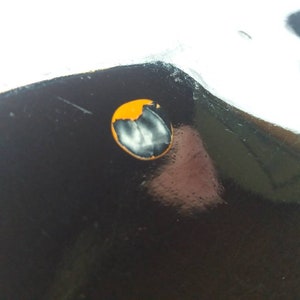 May include: A close-up of a black surface with a small, round, orange sticker with a white design in the center.
