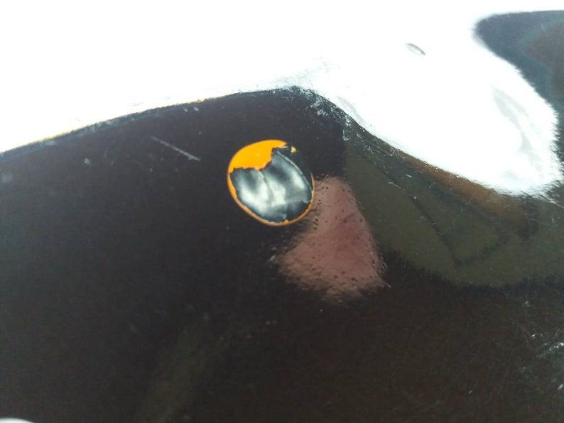 May include: A close-up of a black surface with a small, round, orange sticker with a white design in the center.