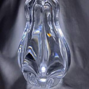 Könnte beinhalten: Eine klare Glasvase mit einem einzigartigen, wellenförmigen Design. Die Vase ist birnenförmig und hat eine breite Öffnung oben.