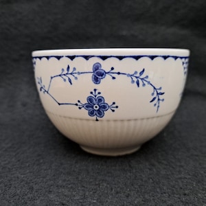 May include: A white ceramic bowl with a blue floral design. The bowl has a scalloped blue rim and vertical ribbed detailing on the lower half. The floral pattern includes stylized flowers and leaves.