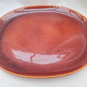 Puede incluir: Un plato de servir ovalado grande con un glaseado brillante marrón rojizo. El plato tiene un borde ligeramente elevado y una superficie lisa y uniforme.