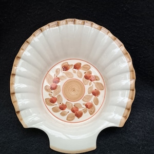 Może przedstawiać: Biała ceramiczna miska w kształcie muszli z brązową krawędzią. Miska ma brązowy i czerwony wzór kwiatowy z kółkiem w środku.