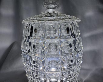 May include: A clear glass candy dish with a geometric pattern and three legs. The dish has a lid with a knob on top.